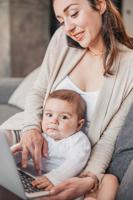 Young Mother Combine Of Child's Care And Remote Working At Home. Woman Talking On Smartphone And Usi