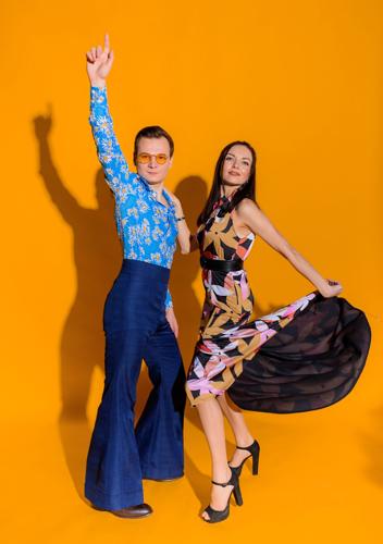 Front view of man and woman dressed in clothing like from 70s on the yellow wall isolated. Couple posing for the photoshoot.
