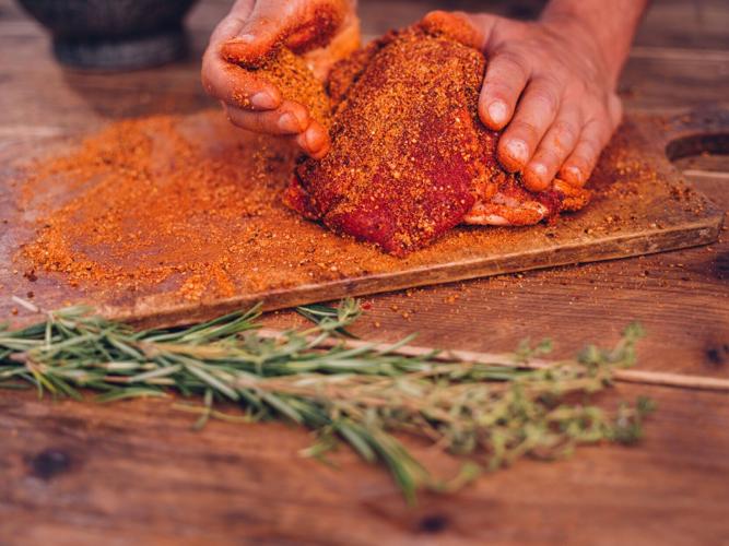 Seasoning of herbs and spices being rubbed into pork