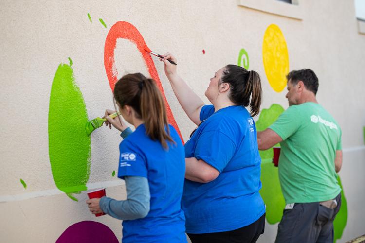 Volunteers paint mural on front of Facing Hunger Foodbank during United