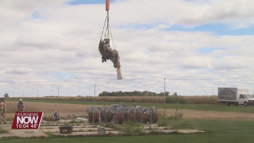 Power line workers soar through the sky hanging from a helicopter in Allen County