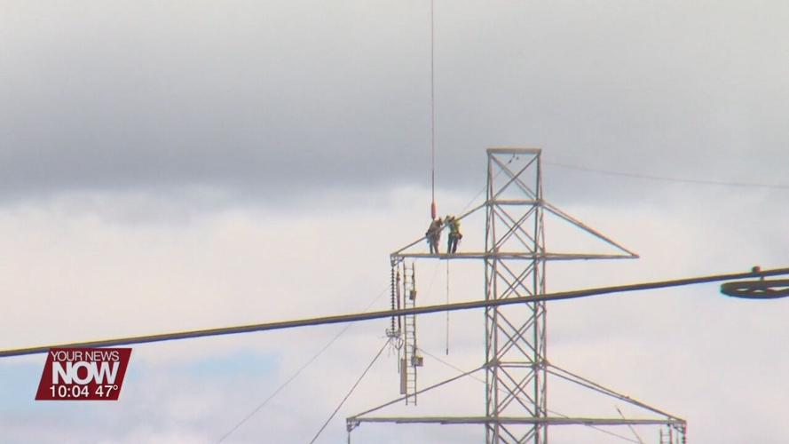 Power line workers soar through the sky hanging from a helicopter in Allen County