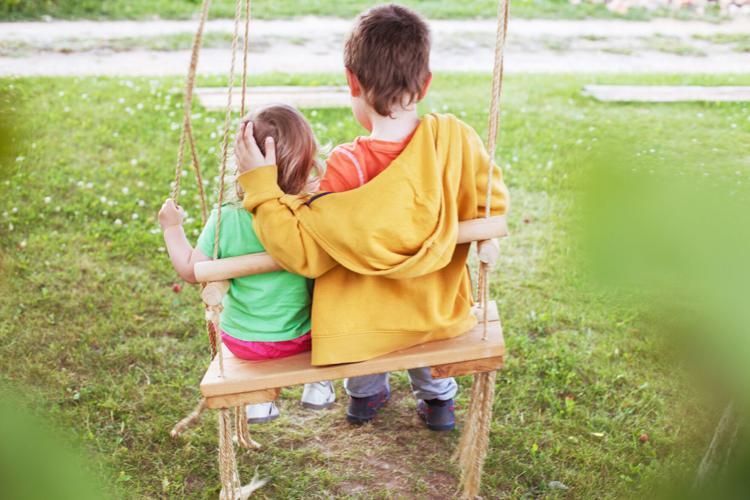children sitting on a swing in the garden. older brother hugging little sister