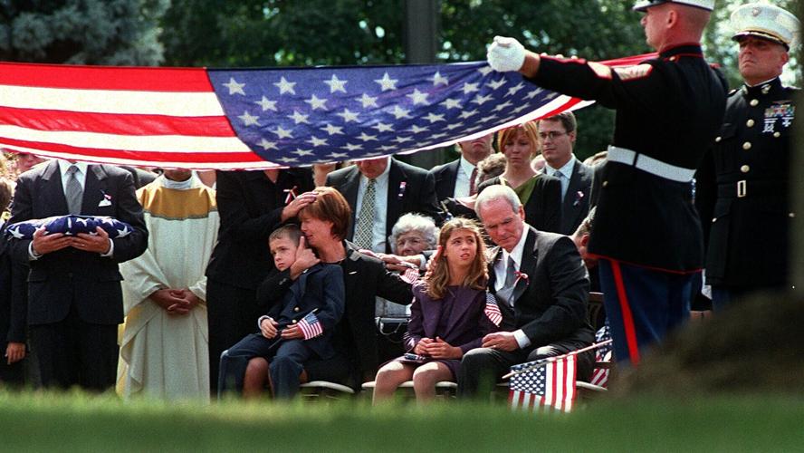 Miriam Horrocks, middle left, cradles her son Mick, 6, as her father-in-law William Horrocks, middle right, sits with her daughter Christa Horrocks, 9, as a U.S. Marine Corps Honor Guard folds up a U.S. flag following a memorial mass and service for her...