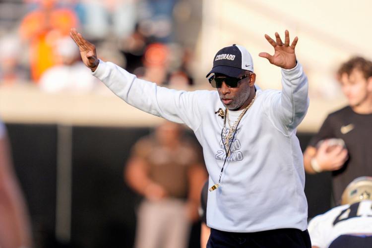 Colorado coach Deion Sanders stands on the field as the team warms up before a college football game between the Oklahoma State