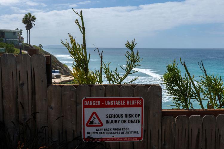A sign warning of bluff failure is displayed on a fence along a sandstone bluff in Encinitas