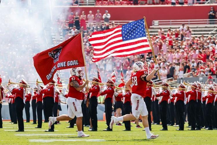 Sep 6, 2025; Raleigh, North Carolina, USA; North Carolina State Wolfpack defensive end Colby Cronk (58) runs with the American flag while defensive lineman Joseph Castaneda (97) runs with North Carolina State Wolfpack flag before the first half of the g...