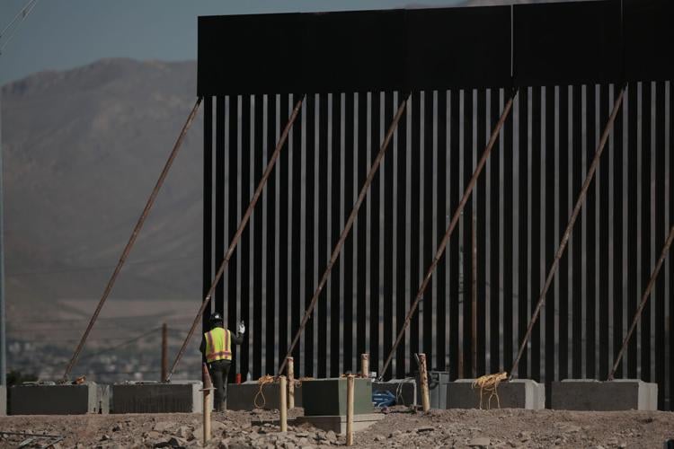 Workers use cranes and heavy machinery to install iron panels for a new black border wall along the banks of the Rio Grande,