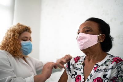 Nurse applying vaccine on patient's arm using face mask