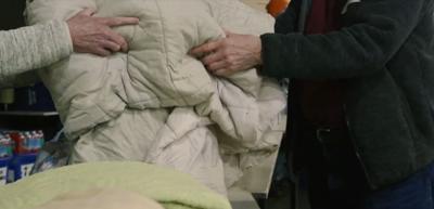the hands of two people in jackets pass a large white blanket