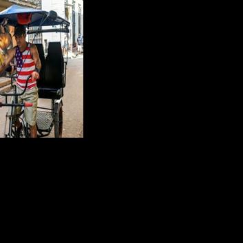 A man wearing a US-flag designed T-shirt rides his tricycle along a street in Havana