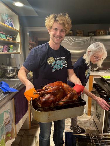 Daniel Dreifuss holds up a freshly cooked turkey that he was in charge of preparing as his mother, Sally Silvers, helps with the oven.