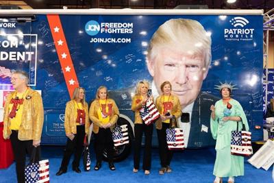 Attendees wearing MAGA merch stand next to an image of Trump at the Conservative Political Action Conference in Grapevine, Texas, on March 25, 2026.