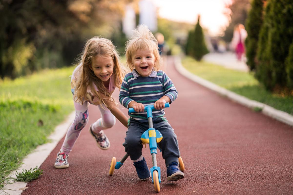 Happy boy having fun on tricycle while his sister is pushing him.
