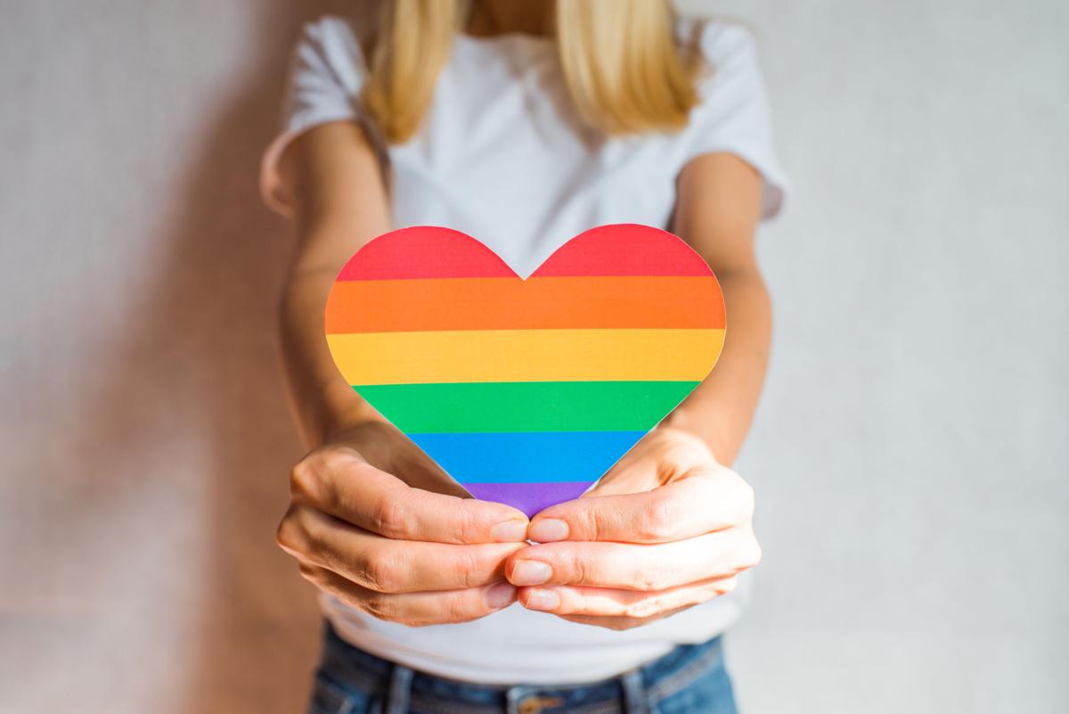 Woman holds in hands a heart in the colors of the rainbow. Young beautiful girl. LGBT history month. Pride Month. Lesbian Gay Bisexual Transgender. LGBT flag. Love, human rights, tolerance. LGBTQ+