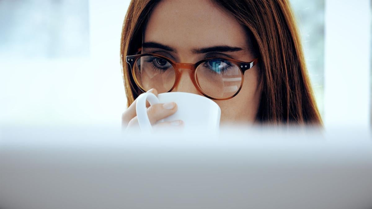 Computer and coffee, woman wearing glasses.