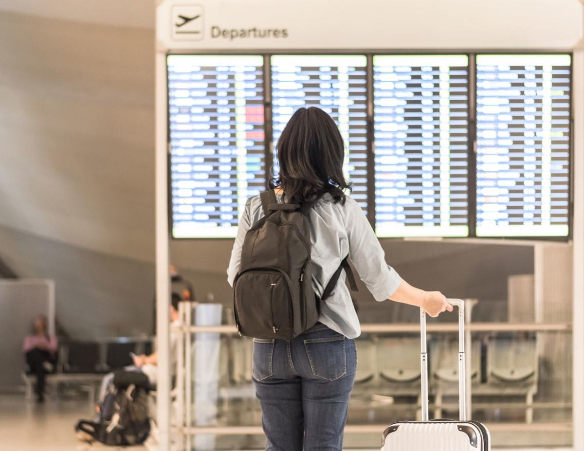 Passenger traveling with luggage and backpack at the flight information board in airport terminal waiting hall area checking time for departure-arrival and delay flight status