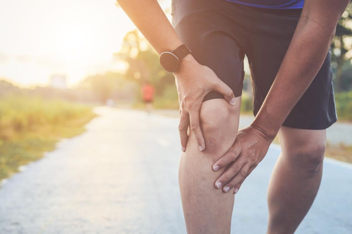 Midsection Of Man Holding Knee While Jogging In Park