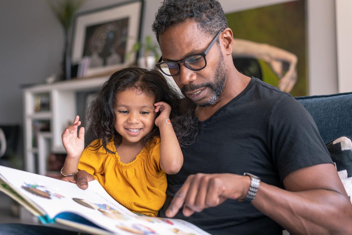 Affectionate father reading book with adorable mixed race daughter