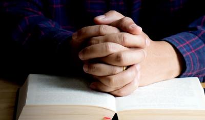 Hands of praying young man and Bible on a wooden table.