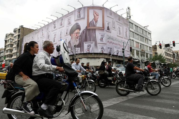 People ride motorcycles near a billboard featuring an image of the late Supreme Leader of Iran, Ayatollah Ali Khamenei, in Tehran