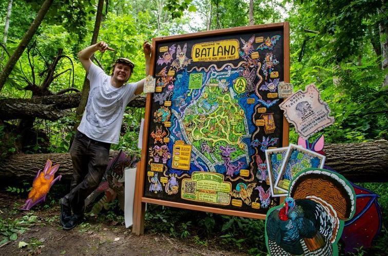 Artist Spencer Beals poses beside the Batland trail map and interactive art installations in Asheville on July 22, 2026.