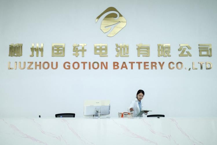 A woman stands next to a logo of Chinese battery maker Gotion, in Liuzhou