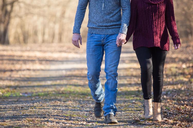 Young caucasian couple walking on dim gravel, dirt, rural, country road holding hands, kissing,smiling, laughing in love having fun season late winter bare trees