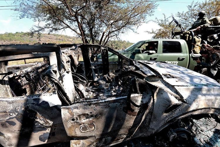 Members of the army onboard a truck are seen next to a burned car used to block roads while Mexican drug lord "El Mencho" tried to flee, near the " Tapalpa Country Club", where he was hiding at the moment of the operation in which he was killed, in Tapa...
