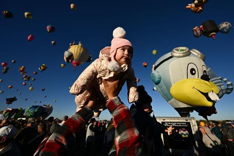 TOPSHOT- Clarissa is lifted into the air by her father as hot air balloons take flight at sunrise during the Albuquerque International Balloon Fiesta in Albuquerque, New Mexico on October 13, 2023.