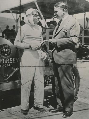 (From left) Three time Indy 500 winner, Wilber Shaw holds an early racing helmet while chatting with Barney Oldfield “The Speed King,” at the Legion Ascot Speedway in California. Shaw used his experience working at Firestone to help develop synthetic ru...