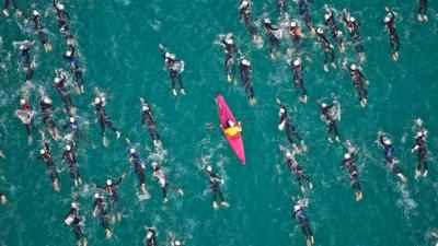 A kayaker paddles among swimmers