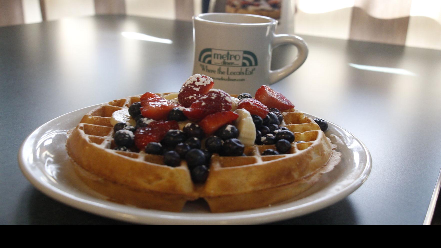 Waffles with blueberries, strawberries and bananas. ThEre is also a mug in the behind