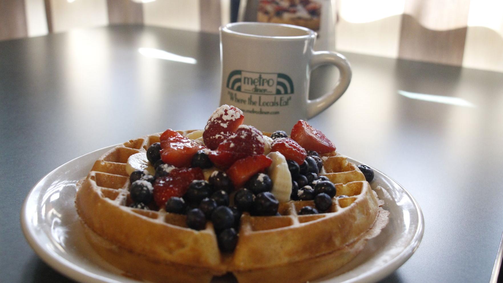 Waffles with blueberries, strawberries and bananas. ThEre is also a mug in the behind