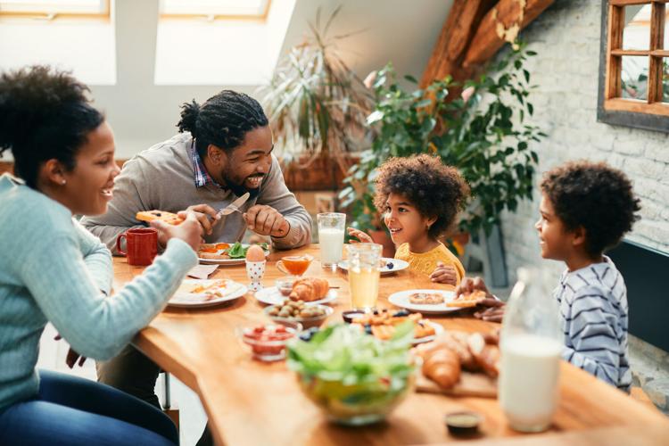 Happy African American family enjoying in conversation while eating breakfast together at dining table.