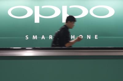 FILE PHOTO: A commuter using his mobile phone passes an advertisement of Chinese smartphone maker Oppo at a train station in Singapore
