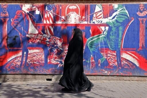 A woman walks past an anti-US mural depicting Iran-US talks near the former US embassy in Tehran