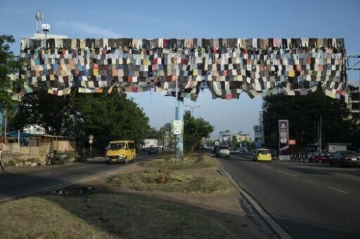 Cars drive under a billboard covered with clothes as part of the 'Baleboard' project in Accra
