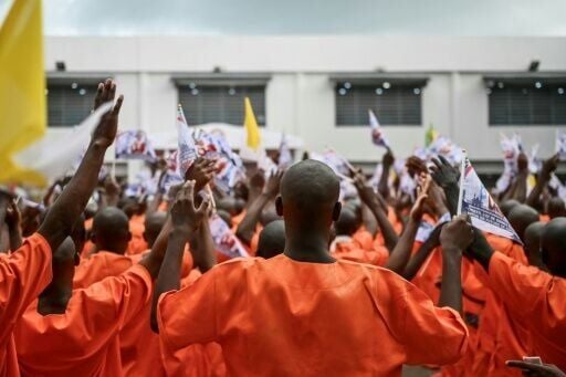 Inmates pray and wave flags bearing images commemorating the visit of Pope Leo XIV during his visit to Bata Prison