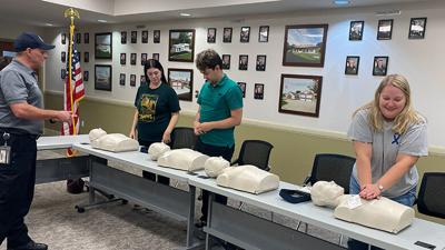 Kenny Strathmann, chief operations officer at Joachim-Plattin Ambulance District, talks as Leader staff members, from left, Ashley Drennen, Carrson McDaniel and Abby Stetina practice CPR.