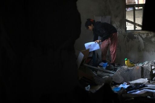 A Palestinian girl picks up her school work from the debris of a destroyed house