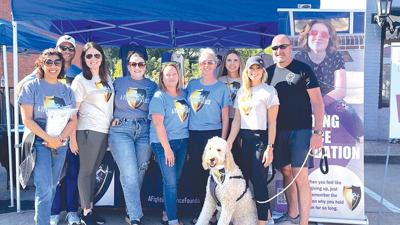 A banner with Camryn Tripp’s photo is in the background as members of A Fighting Chance Foundation pose for a photo at their Twin City Days booth.
