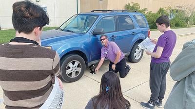 Students in the “Adulting 101” class watch as high school security officer Rowdy Schmoll shows how to change a tire.
