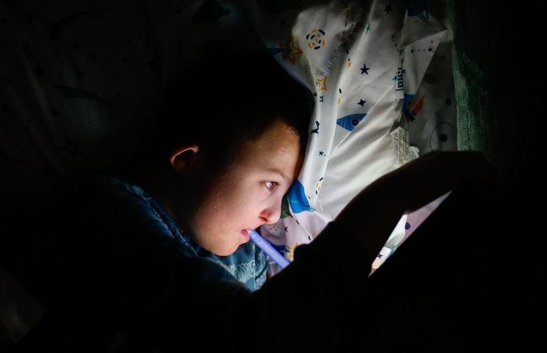 Carter lies in bed watching videos on his iPad before going to sleep
