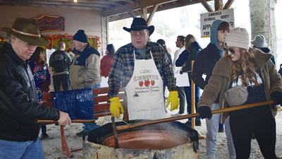 Apple Butter volunteers David Brock and Greg Pfeiffer show Amy Woods of Eureka the proper way to stir apple butter in the wood-fired kettle.
