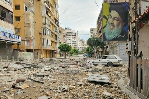 A banner bearing the image of Hassan Nasrallah, the assassinated leader of the Lebanese Shia movement Hezbollah, hangs from a building along a street littered with debris at the site of an overnight Israeli airstrike in Beirut on March 25, 2026