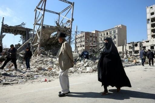 A man and a woman walk past destroyed buildings following airstrikes in central Tehran, on March 4, 2026