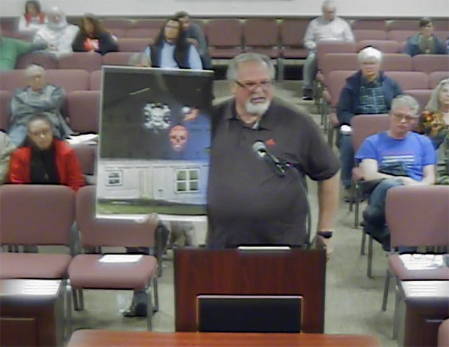 Dan Ross Jr. holds up an image of two skulls projected onto the side of the sober living home.