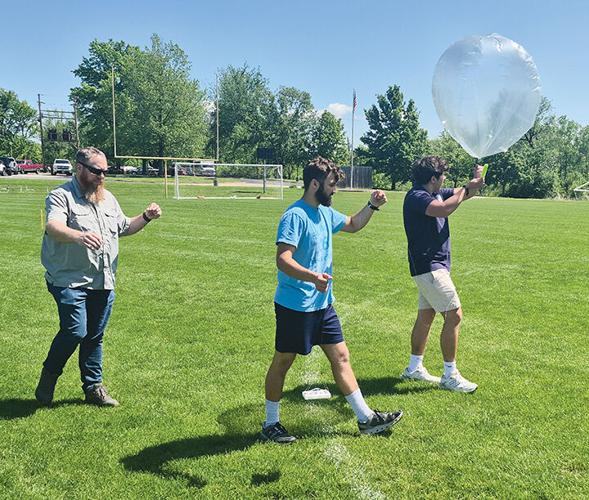 From left, Travis Few, a Midwest High-Altitude Balloon Team flight lead; Alvaro Mejias and Abram Brooks carry the St. Pius X High School Amateur Radio Club’s balloon on May 6 to its launch point on the school’s football field.