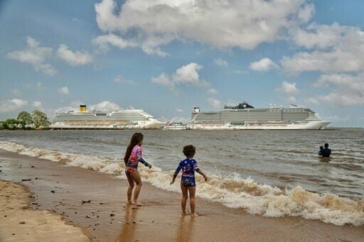 Children bathe on a beach along the Guamá River with cruise ships seen in the background docked at the Port of Outeiro